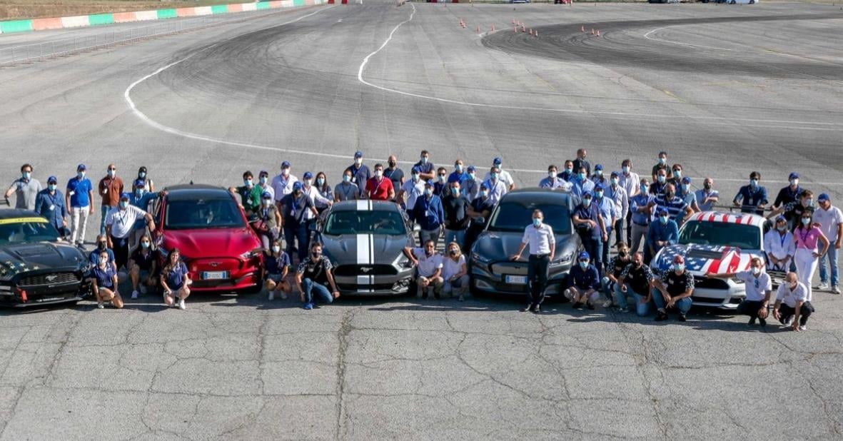 Gruppo di persone in posa con auto sportive schierate in pista