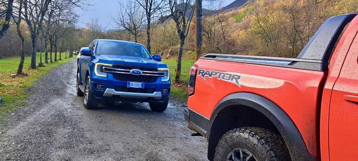 Ford Ranger blu e Ford Raptor rosso su un viale alberato, colline autunnali